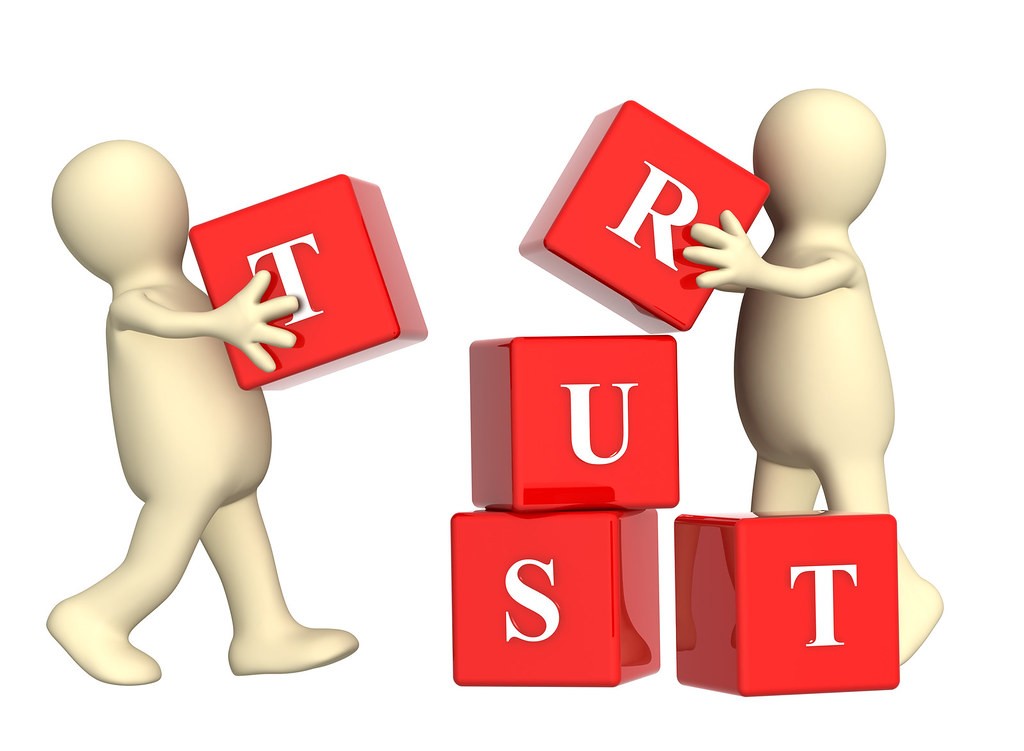 Two featureless people building the word Trust with building blocks
